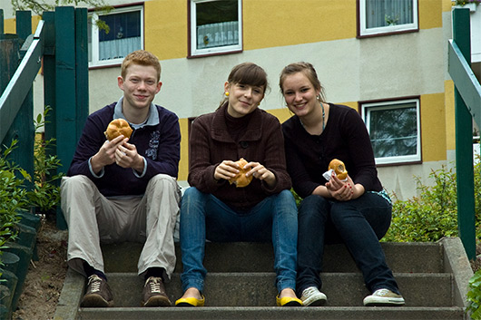 Drei Jugendliche beim Bratwurstessen auf der Treppe im Außenbereich der Kirche