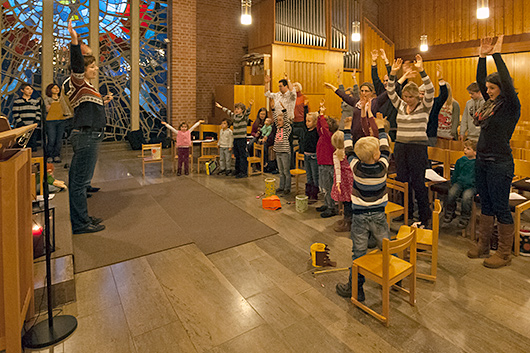 Blick in den Kirchenraum, wo die Kinder und ihre Angehörigen mit Bewegungen ein Lied begleiten.