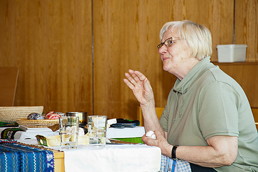 Marianne Bieker erläutert, am Tisch sitzend, wie die farbigen Ostereier hergestellt werden.