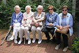 Fünf Teilnehmerinnen des Seniorenausflugs sitzen vor Fahrtbeginn auf der Bank vor der Trinitatiskirche.