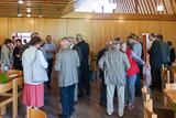Blick in den großen Gemeinderaum, wo zahlreiche Besucherinnen und Besucher des Gottesdienstes in Gespräche vertieft sind.