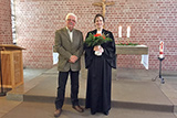 Pfarrerin Mohr und Heinz Rau stehen vor dem Altar der Trinitatiskirche, wo der stellvertretende Vorsitzende des Kirchenvorstands der Pfarrerin einen Blumenstrauß überreicht hat.