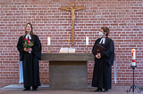 Die beiden Pfarrerinnen stehen links und rechts vom Altar und blicken in Richtung Kirchenraum.