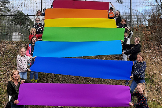 Kinder haben sich an einem Hang im Außenbereich der Trinitatiskirche mit Kreppbahnen in Regenbogenfarben aufgestellt.