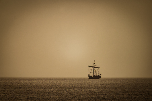 Ein in der Ferne erkennbares altertümlich aussehendes Segelschiff fährt einsam auf dem Stettiner Haff.