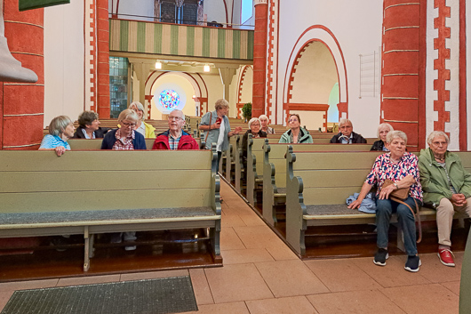 Die Teilnehmer*innen am Ausflug im Rahmen des Gemeindetreffs sitzen auf den Kirchenbnken der Nikolaikirche in Caldern und hren den Ausfhrungen von Pfr. Ruckert zu.