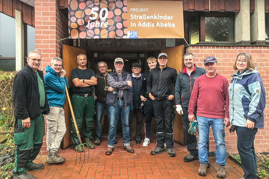 Die Mitwirkenden an der Gartenaktion 2024 haben sich vor dem Eingang zur Trinitatiskirche zum Gruppenbild aufgestellt. Ein Transparent ber dem Eingang weist auf das 50-jhrige Bestehen des Straenkinder-Projekts hin.