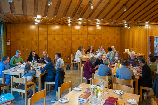 Blick in den groen Gemeinderaum, wo die Besucherinnen und Besucher des Gottesdienstes am Grndonnerstag an Tischgruppen sitzen und sich angeregt unterhalten.