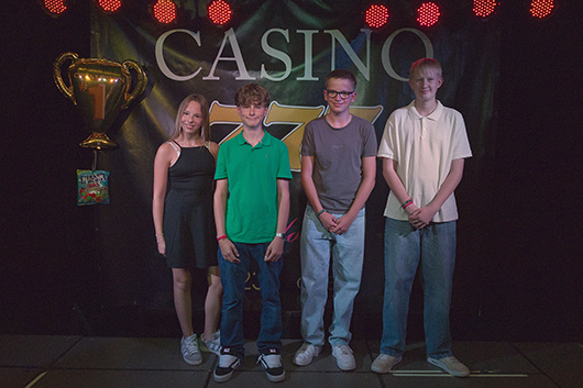 Eine Konfirmandin und drei Konfirmanden haben sich zum Gruppenbild vor einer Banner aufgestellt, das mit CASINO überschrieben ist.