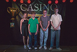 Eine Konfirmandin und drei Konfirmanden haben sich zum Gruppenbild vor einer Banner aufgestellt, das mit CASINO berschrieben ist.