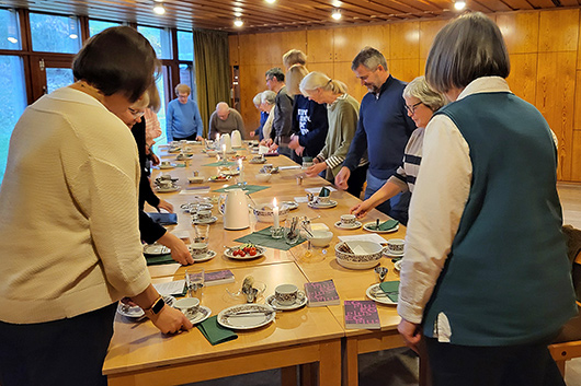 Nach dem Tischabendmahl erheben sich ie Teilnehmer*innen von ihren Pl�tzen im gro�en Gemeinderaum, um mit dem Abr�umen zu beginnen.